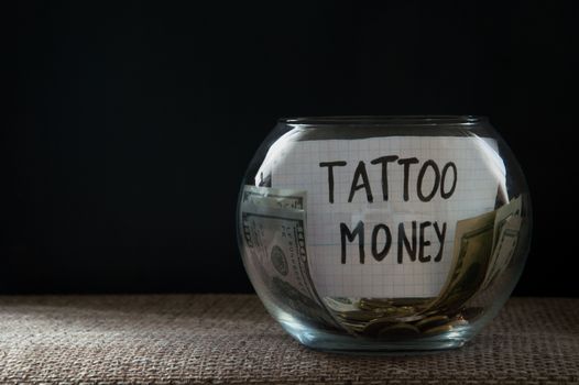 Glass jar witn money for tattoo on black background