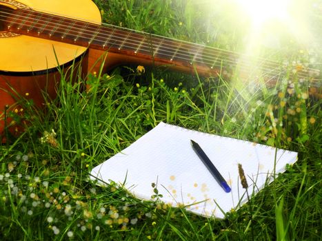 Photo of guitar and notepad with pen on the grass