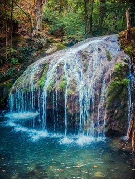 Waterfall from ravine with bright clear water in forest