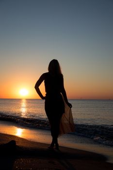 Young woman standing on sand near sea and looking to a sun