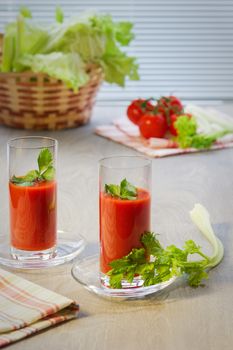 Two glasses with tomato juice, tomatoes, stalks and leaves of a celery on a table in style a rustic