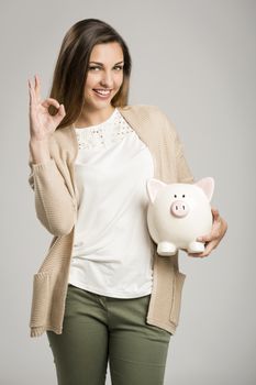 Beautiful and happy woman holding a piggy bank, isolated over white background