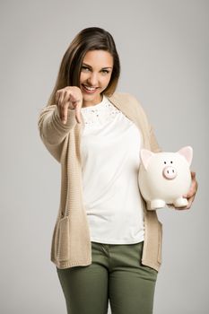 Beautiful and happy woman holding a piggy bank and pointing to the camera