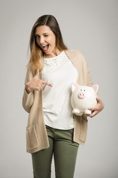 Beautiful and happy woman holding a piggy bank and pointing to it