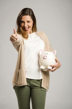 Beautiful and happy woman holding a piggy bank and making thumb up