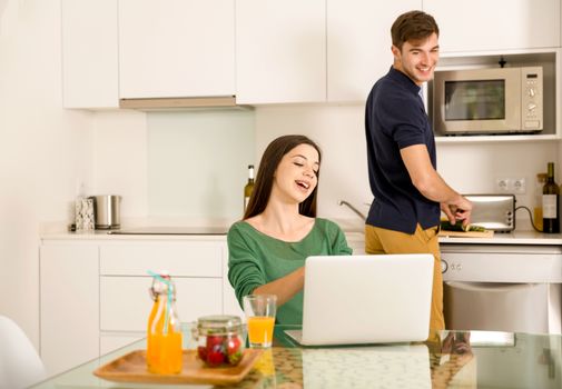 Man cooking while her wife working on a laptop