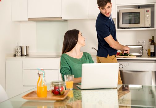 Man cooking while her wife working on a laptop