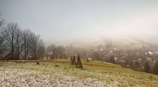 Late autumn misty morning in a village. First Snow in mountains