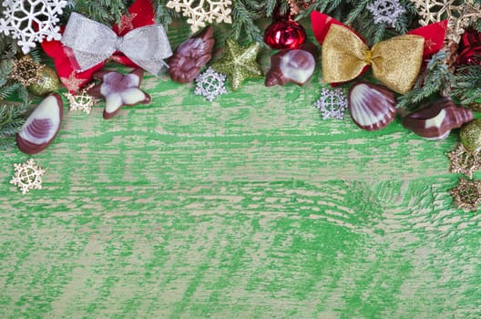 Christmas green background on the old wooden surface, plenty of space for labeling. Sprigs of juniper,jewelry, wood and chocolate.Painted in green.