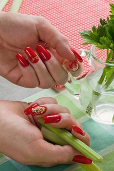 Female hands with bright manicure hold a jug with water and greens