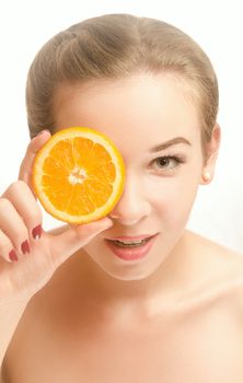 Portrait of an attractive young woman with a slice of orange in front of her eyes, which stands on white background and smiling