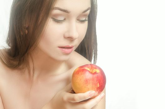 Young tender woman holding a peach in her hand with downcast eyes. White background