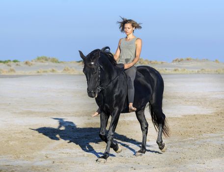 horse woman galloping with her black stallion on the beach