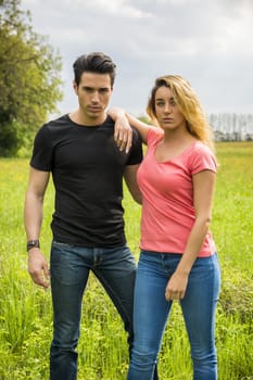 Boyfriend and girlfriend standing in countryside in green luscious field, embracing each other and cuddling, showing romantic love