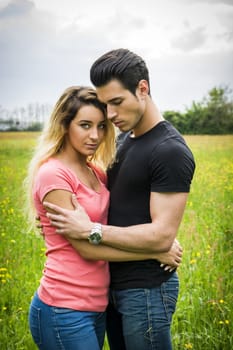 Boyfriend and girlfriend standing in countryside in green luscious field, embracing each other and cuddling, showing romantic love