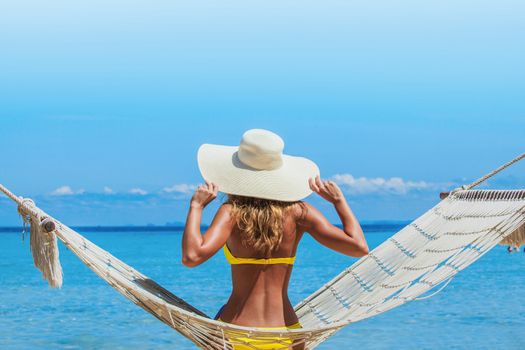 Woman in sunhat swinging in hummock on blue sea background