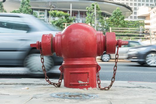 red fireplug standing alone on footpath/motion blur car background.