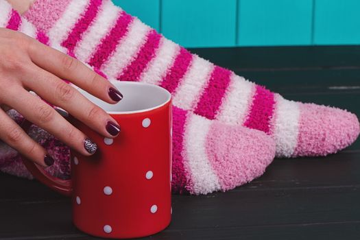 Comfort Concept - Woman drinking hot cocoa. Close-up of female legs in bright colored warm socks