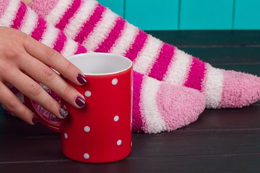 Comfort Concept - Woman drinking hot cocoa. Close-up of female legs in bright colored warm socks