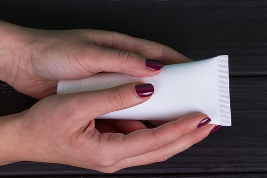 Woman's beautiful hands with care cream tube on the black background