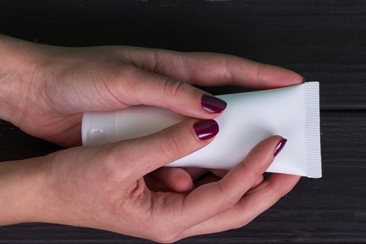 Woman's beautiful hands with care cream tube on the black background
