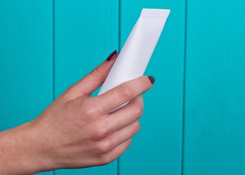 Woman's beautiful hands with care cream tube on the blue background
