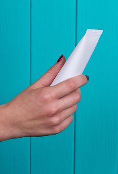 Woman's beautiful hands with care cream tube on the blue background