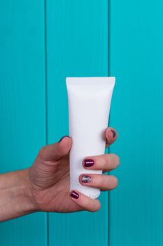 Woman's beautiful hands with care cream tube on the blue background