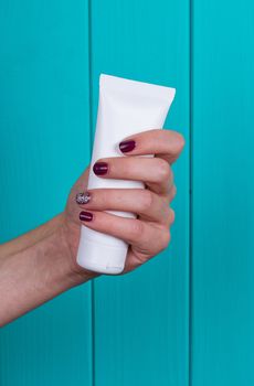 Woman's beautiful hands with care cream tube on the blue background