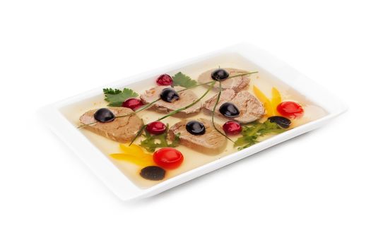 The jellied meat served on a white dish with segments of yellow sweet pepper, tomatoes, olives, parsley and leaves of the arugula isolated on a white background.