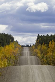 Autumn along the adventurous rise and fall of Cassiar-Stewart Highway in British Columbia. Vertical photograph with copy space in sky. Rambling road travel symbol.  Date is September 6, 2015. 