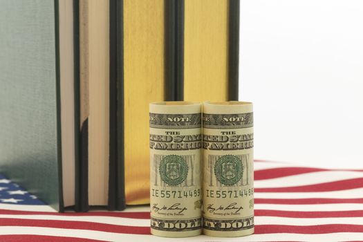American currency in front of books on stars and stripes pattern. Symbols reflect issues of cost, investment needs, and governmental policy related to education. 
