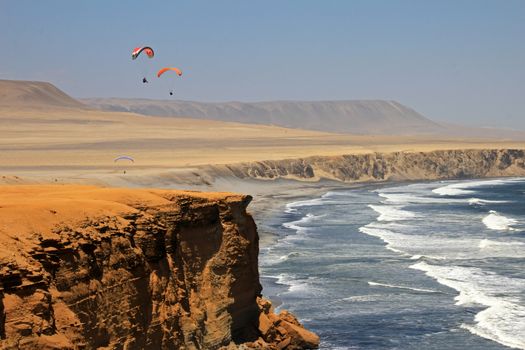 Paraglider soaring over the cliffs at oceanfront of Paracas Peru