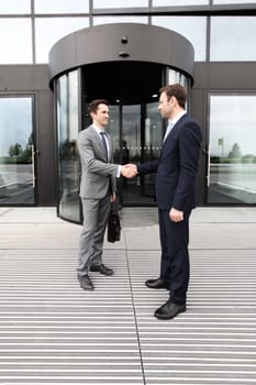 Two businessmen shaking hands in front of office building
