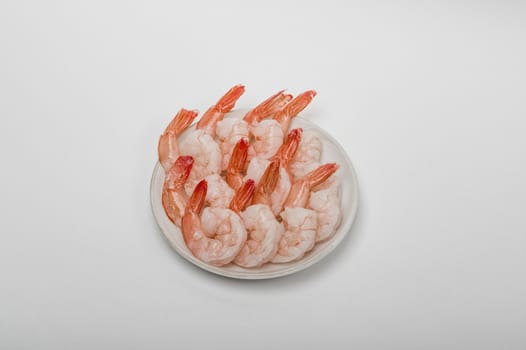 Red peeled prawns lie on a saucer isolated on white background