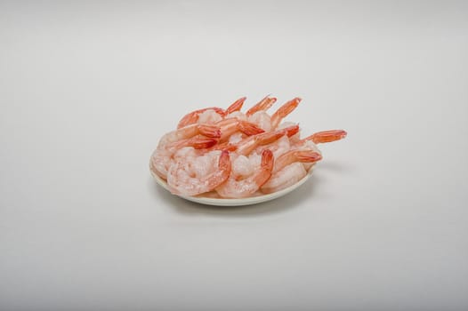 Red peeled prawns lie on a saucer isolated on white background