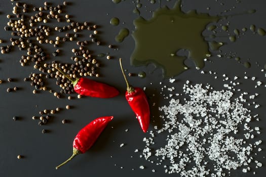 Chili peppers, oil, salt and pepper over a dark background seen from above
