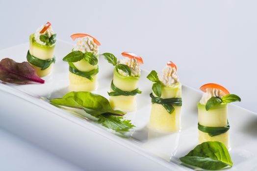 Beautifully decorated fresh squash rolls with soft cheese on plate on light background