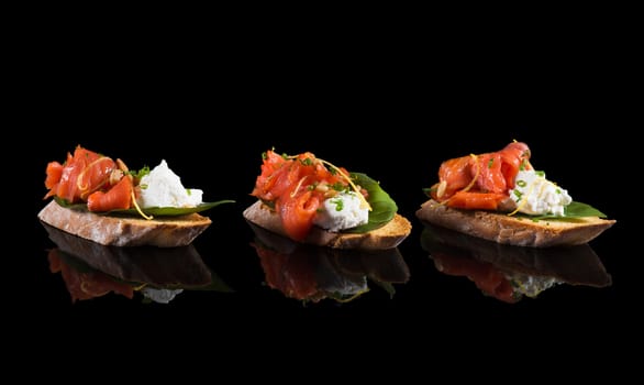 Bruschetta with salmon and soft cheese on black background