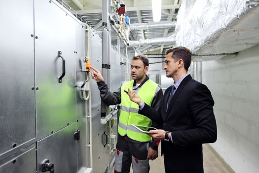 Worker and manager in electrical switchgear room of CNC plant