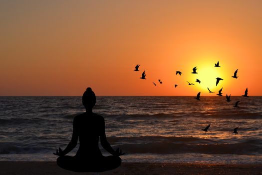 Woman meditating in a yoga pose on the beach at sunrise