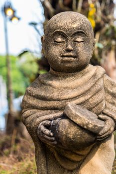 Old statue of a little monk standing and holding monk's alms-bowl