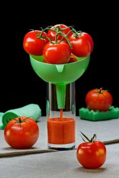 Tomatoes in a funnel in a glass with tomato juice on a table