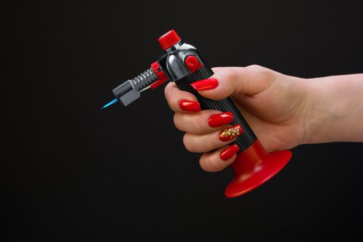 The female hand with beautiful manicure holds a gas torch
