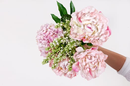 Hand holding a bouquet of different flowers on an isolated studio background