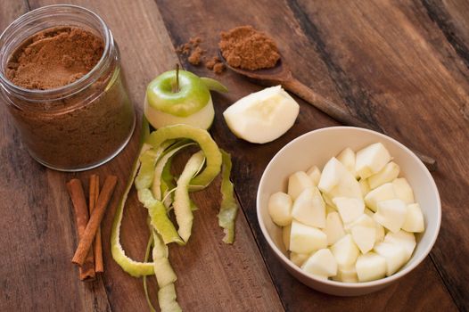 Ingredients for homemade apple sauce with peeled and diced fresh green cooking apples , stick cinnamon and aromatic ground spice for seasoning on a wooden table