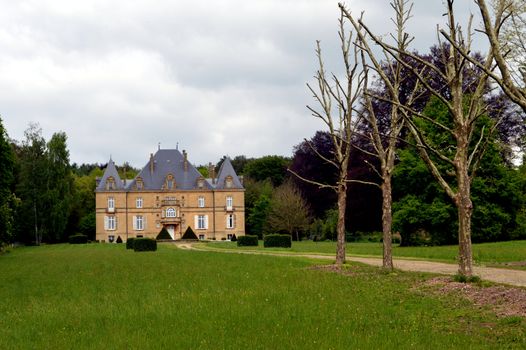 Former castle in the forest with a path of trees and a big lawn.