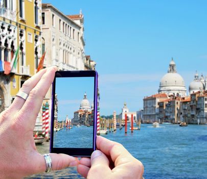 View over the mobile phone display during taking a picture of water canal in Venice. Holding the mobile phone in hands and taking a photo of Venice. Focused on mobile phone screen.
