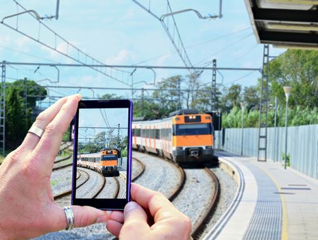 View over the mobile phone display during taking a picture of arriving train at railway station. Holding the mobile phone in hands and taking a photo. Focused on mobile phone screen.