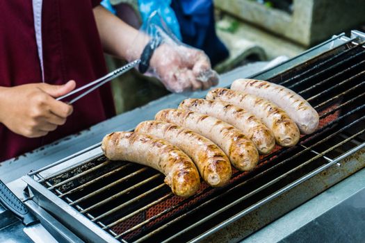 Fresh sausage and hot dogs grilling outdoors on a gas barbecue grill.